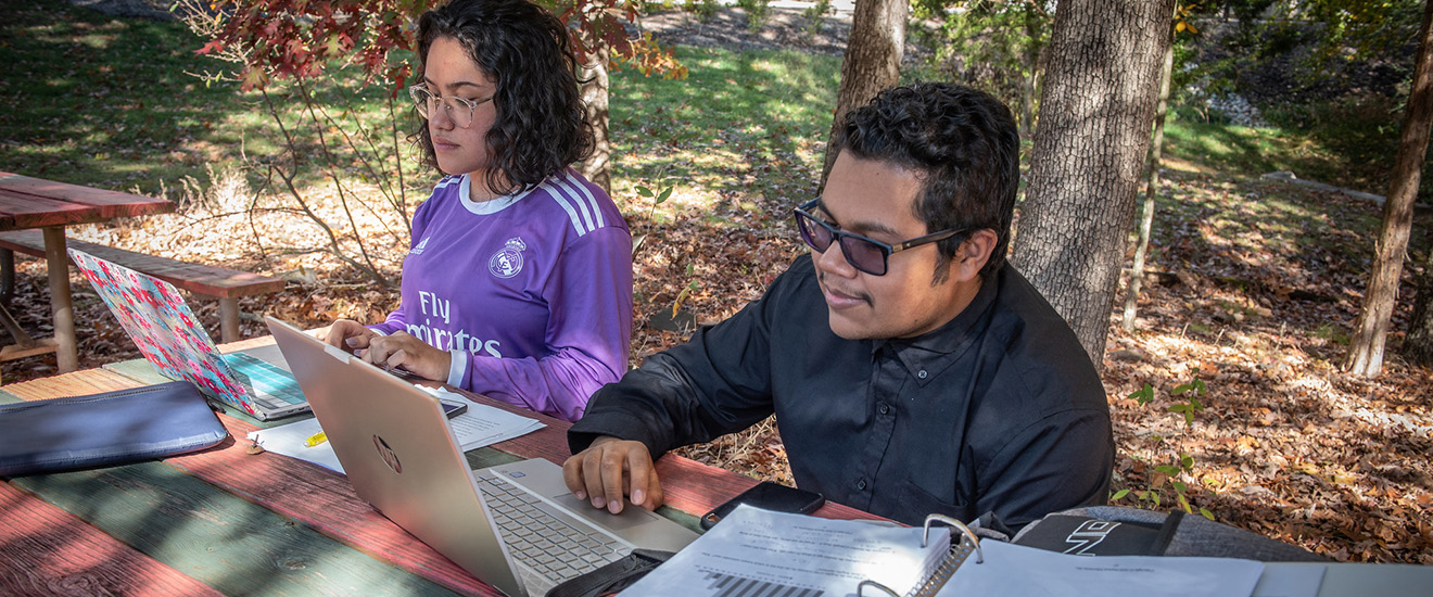 Students working on laptops at a picnic table outdoors